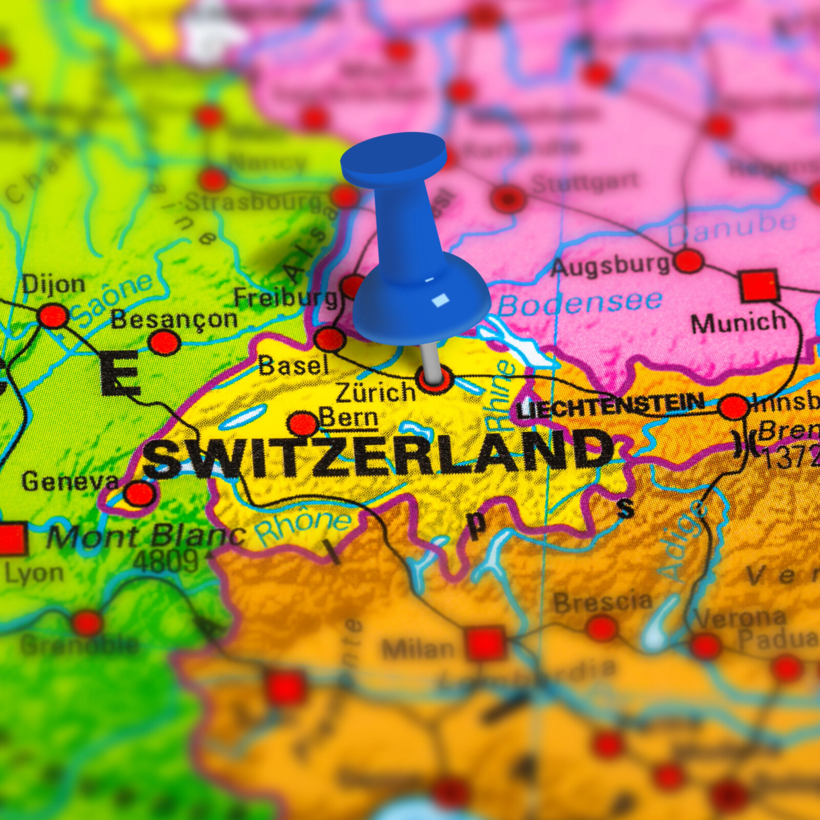 Eine farbige Landkarte, in der Mitte in gelb die Schweiz mit einer blauen Stecknadel
